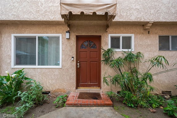 Front view of a house with a brown door and windows on a textured exterior wall.