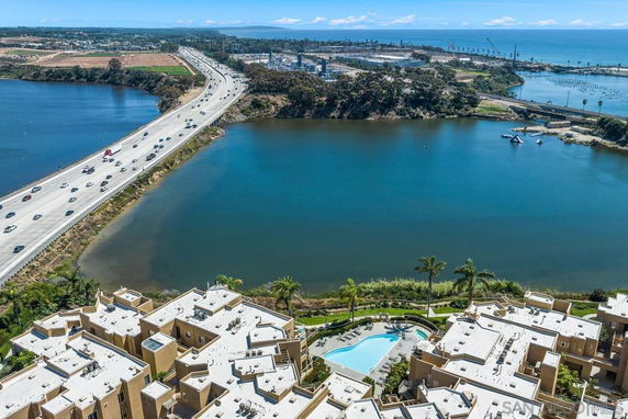 Aerial view of a complex with a pool, overlooking a large body of water and a highway.