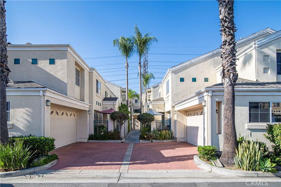 Front view of multiple two-story houses with attached garages and palm trees.
