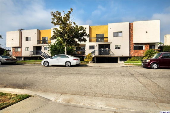 Front view of a modern multi-story building with a tree and parked cars in front.