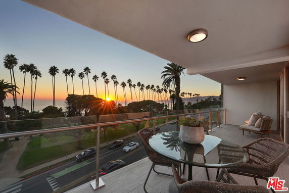View from a balcony overlooking palm trees and the ocean at sunset.