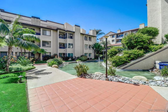 Front view of a multi-story apartment building with a landscaped area and water feature.