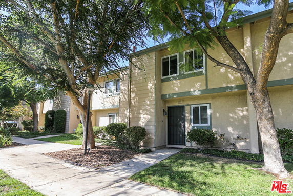 Front view of a two-story apartment building with trees and a walkway.
