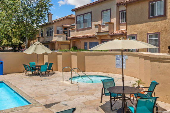 Outdoor swimming pool area with seating and parasols in front of a residential building.
