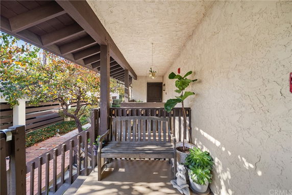Covered porch with wooden bench and potted plants, adjacent to a tree-lined walkway.
