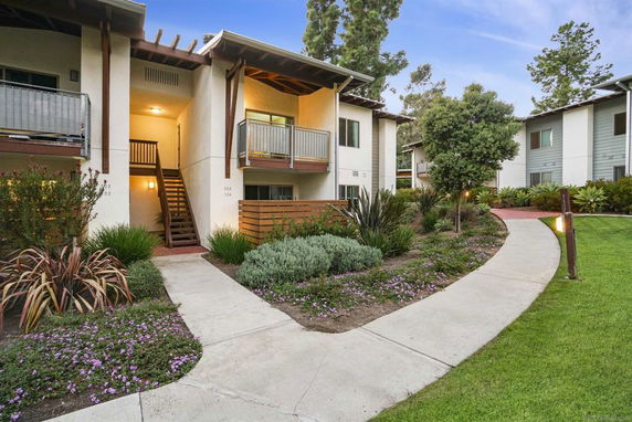 Front view of a multi-story residential building with balconies and landscaped surroundings.