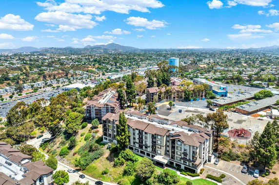 Aerial view of a residential complex surrounded by greenery and a cityscape in the distance.