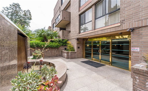 Front view of a multi-story brick building with glass doors and surrounding plants.