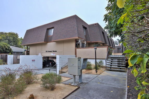 Front view of a two-story building with a brown and beige facade, featuring a driveway and stairs leading to the entrance.