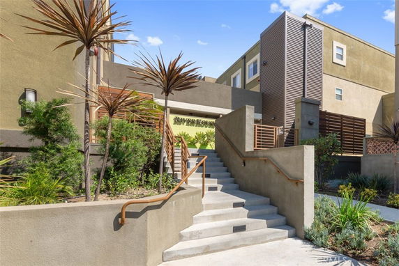 Front view of a modern multi-story apartment building with stairs leading to the entrance.