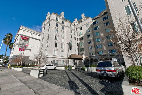 Front view of a multi-story apartment building with a gated entrance and driveway.