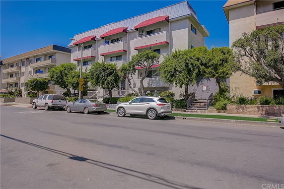 Front view of a multi-story residential building with balconies and metal roof.