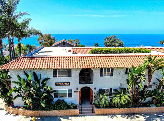Front view of a two-story building with tiled roof and arched entrance, labeled Woods Cove Condominiums.