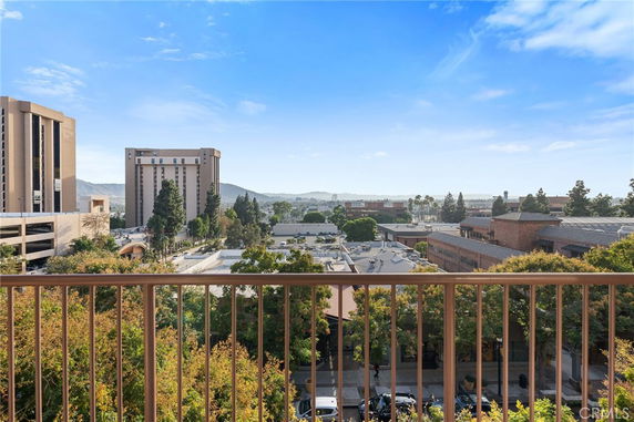 View from a balcony overlooking buildings and trees with hills in the background.