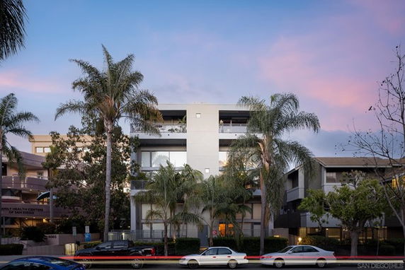 Front view of a modern multi-story building with balconies and palm trees in front.