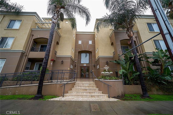 Front view of a multi-story residential building with palm trees and a staircase leading to the entrance.
