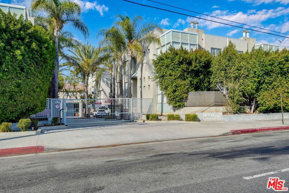 Front view of a multi-story building with gated entrance and palm trees.