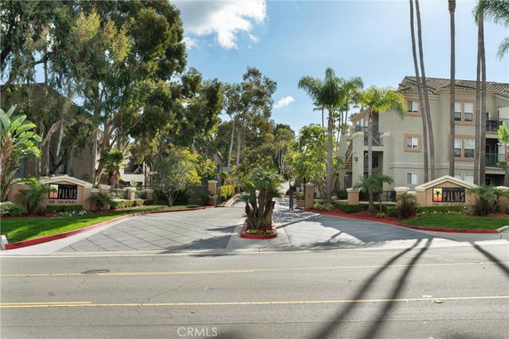 Front view of a multi-story apartment building with palm trees and entrance signage.