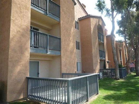 Front view of a multi-story apartment building with balconies and a fenced patio area.