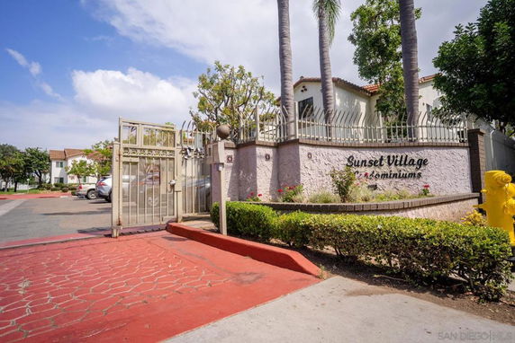 Front view of a condo complex named Sunset Village Condominiums with gated entrance.