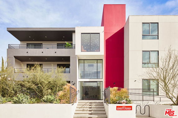 Front view of a modern multi-story building with a unique architecture, featuring a red vertical accent and several balconies.