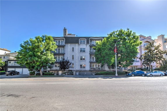 Front view of a multi-story residential building with balconies and green trees on either side.