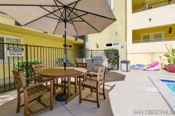 Outdoor swimming pool area with table, chairs, and large umbrella.