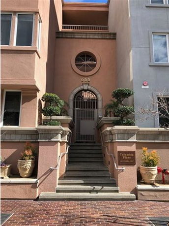 Front view of a multi-story building with stairs leading to a gated entrance.