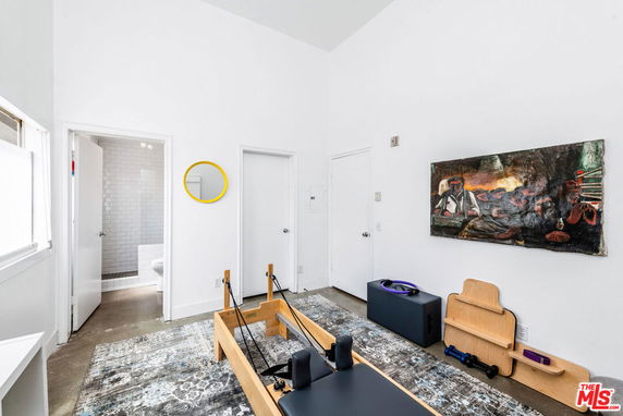 Interior view of a room with exercise equipment, including a Pilates reformer, yoga blocks, and a wall-mounted artwork.