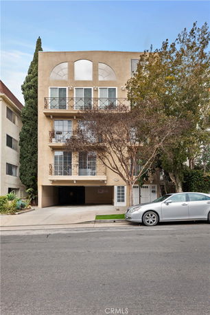 Front view of a multi-story building with balconies and a driveway entrance.