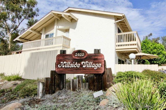 Front view of a two-story building with balconies and a wooden sign saying 'Hillside Village'.