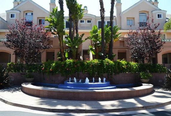 Front view of a multi-story residential building with a fountain and landscaped greenery.