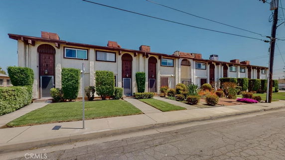 Front view of a row of two-story townhouses with arched doorways and small front gardens.