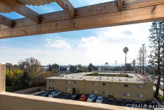View of surrounding areas from a rooftop with wooden beams, overlooking a flat-roofed building and parking lot.