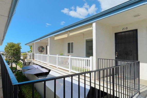 View of an apartment corridor with a railing and visible apartment entrances.
