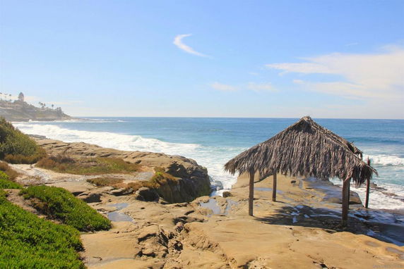 View of a rocky coastline with a thatched hut beside the ocean.