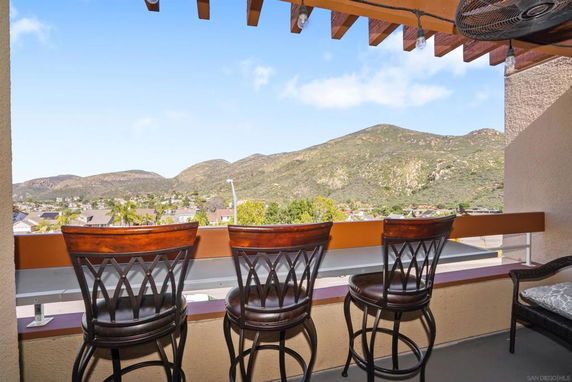 Panoramic outdoor view of mountains and surrounding landscape from a balcony with chairs.