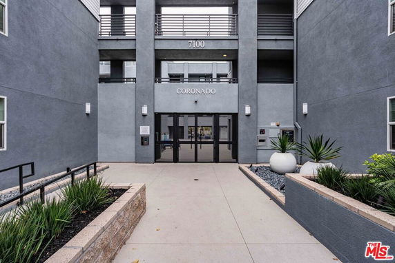 Front view of a modern multi-story building with gated entrance and balconies.