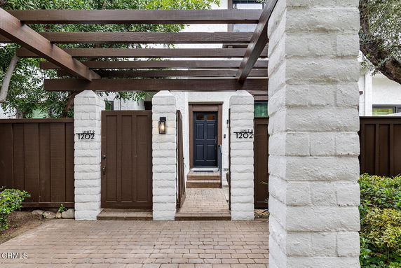 Front view of a house entrance with white brick columns and wooden gate.