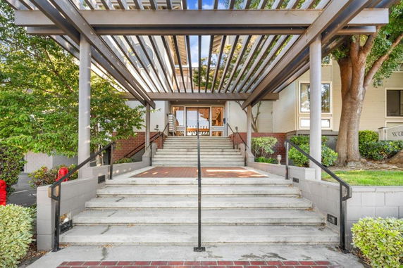 Front view of a building with a pergola over stairs leading to an entrance.