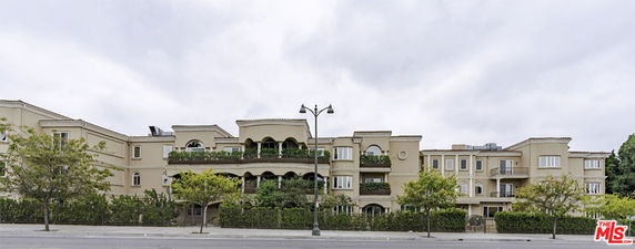 Front view of a multi-story residential building with balconies and green hedges.