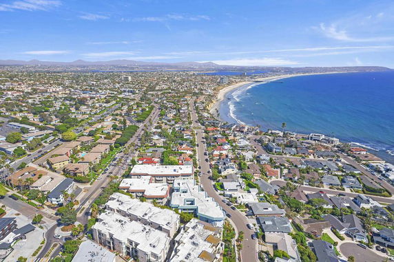 Aerial panoramic view of a coastal residential area with buildings and a shoreline.