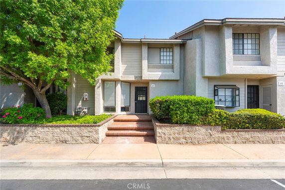 Front view of a two-story townhouse with a small entrance staircase and landscaped shrubs.