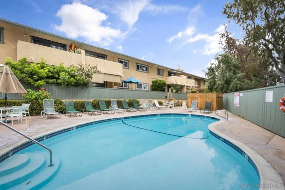 Outdoor swimming pool area with lounge chairs and umbrellas near a two-story building.