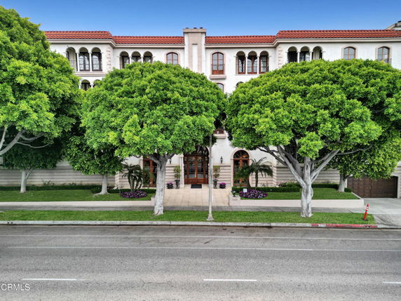 Front view of a multi-story building with an elegant facade and large trees at the entrance.