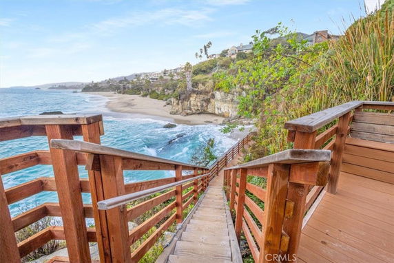 Wooden staircase leading down to a sandy beach with ocean waves and cliffs in the background.