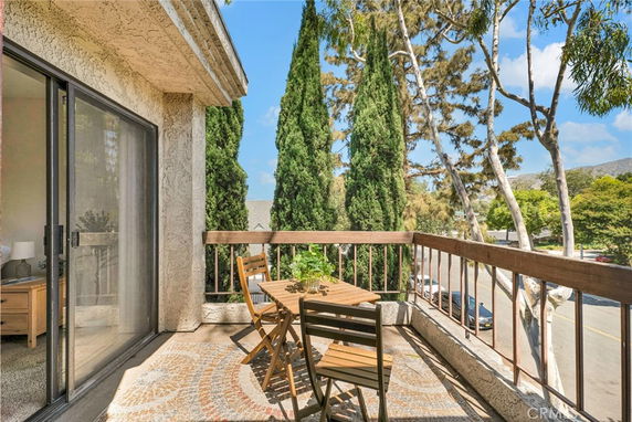 View from a balcony with outdoor furniture overlooking trees and a street.