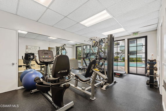 Indoor gym area equipped with exercise machines and a view of a pool outside.
