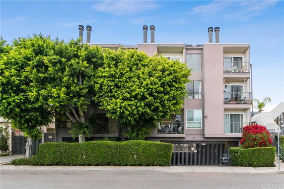 Front view of a multi-story residential building with balconies and surrounding greenery.