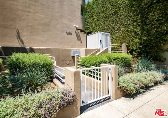 Front view of a building entrance with a white gate and pathway surrounded by greenery.